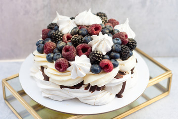 Meringue cake Pavlova with fresh ripe raspberry and blueberry, and whipped cream on grey background.