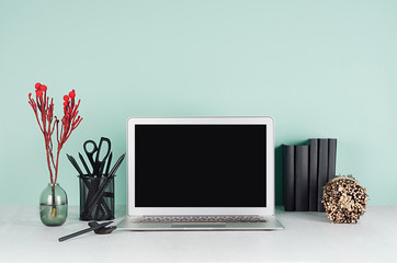 Modern business workplace with blank computer display, black stationery, books, sheaf of dry brown branches, red branch in green mint menthe interior on white wood desk.