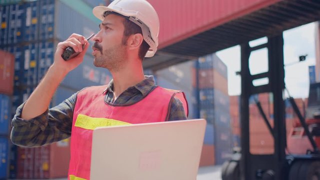 Close Up Technician Or Engineer Worker Use Walkie Talkie Contact With Team Then Typing Laptop And Stand In Cargo Shipping Container Workplace With Concept Of Good Management For Industrial Business.