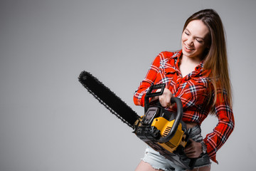 Builder girl with chainsaw in a red shirt on a gray background
