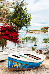 an old blue-white fishing boat lies on the shore, a repair base for boats in Greece, Greek islands in the background, red flowers on white houses on hydra island,