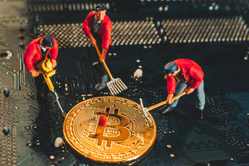 Bitcoin mining miniature worker, small figure holding mattock digging on shiny golden Bitcoin...