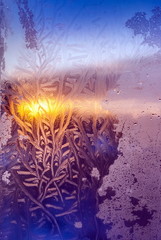 The light of the setting sun through the frosty pattern on the glass in winter