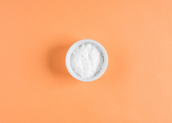Baking soda in bowl on orange background. Concept of baking soda as multi use cleaning or beauty ingredient