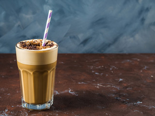 Frappe milk shake coffee in tall glass on blue and brown background. Straw