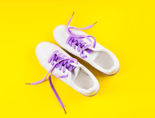 White sneakers with purple laces on yellow and purple split background. Modern minimal fashion art trendy bold color flat lay still life
