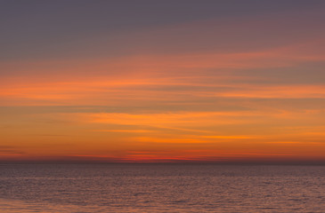 Bright twilight sunset sky over the sea. Wonderful sky after sunset in orange shades. The natural background. Purple hue of the sea and sky. Abstract lines of fire clouds.