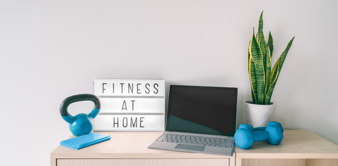 Fitness at home online exercise class on computer laptop with training weights and resistance band. Coronavirus COVID-19 Social distancing sign lightbox banner staying indoor while gyms are closed. - Powered by Adobe