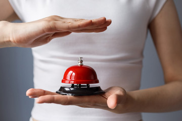 Woman is holding red bell, button on her hand. Girl is going to press the red button, bell. 