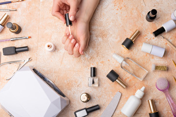 Beauty salon or home manicure. Woman's hands paint gel with varnish on the background of tools.