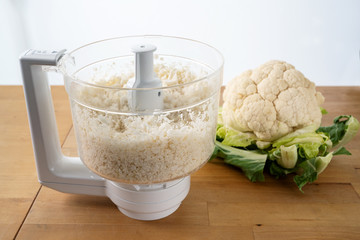 cauliflower shredded in a food processor for healthy low carb pizza crust or as vegetable rice replacement on a wooden kitchen table