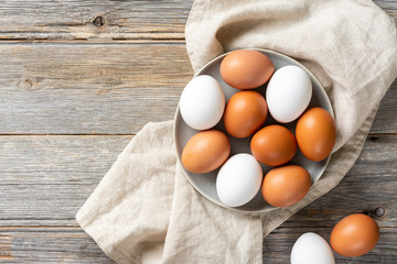 Eggs in a plate on the kitchen table. White and brown eggs for cooking. Chicken eggs on a wooden culinary background. Concept of preparation for baking. Top view with space for text