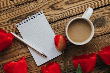 Notebook with white pages and silver pen, red tulips and cup of coffee on the wooden background. Free copy space for text. Planning