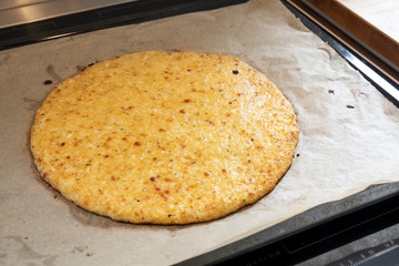 Freshly baked pizza crust from shredded cauliflower and cheese on a baking tray, healthy recipe for slimming with low carb or ketogenic diet, selected focus, narrow depth of field