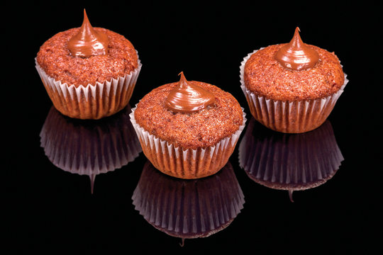 Three chocolate muffins with cream, isolated on black background, with reflection