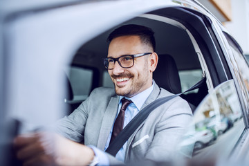 Attractive caucasian smiling elegant unshaven businessman in suit and eyeglasses driving his expensive car.