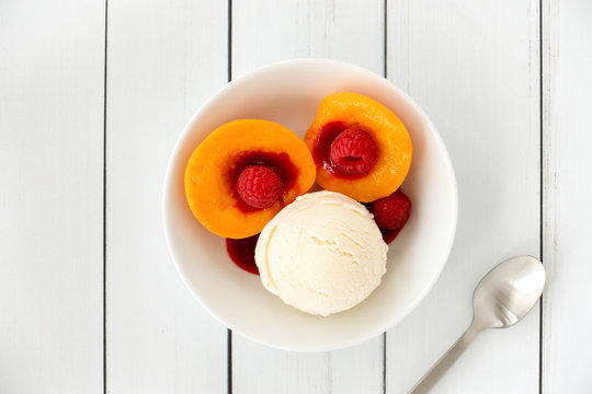 Top View of a Peach Melba Sundae in a Bowl on White Wood Background