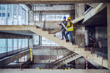 Construction worker and main architect climbing the stairs and talking about progress in construction of new building.