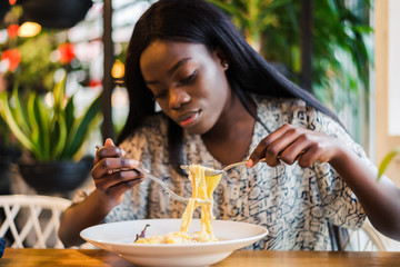 Young african woman eating spaghetti in restaurant