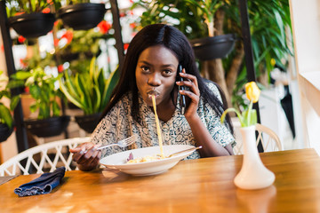 Portrait of young african woman eating spaghetti pasta and talking on the phone