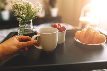 Breakfast on a tray in bed at home white dark linen. croissant tea strawberries