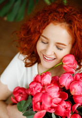 Dreamy curly girl with closed eyes enjoys a bouquet of pink peonies