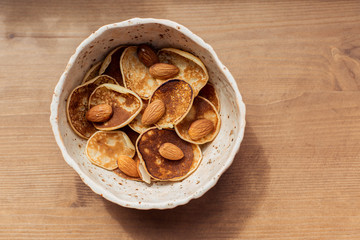 Tiny pancake cereal quarantined trending food. Fun pastry at home for breakfast with nuts and butter on a plate. Grilled homemade food on a wooden table background. Mini Top view place for text 