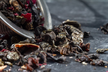 Tea leaves of green and black tea lie in an iron sieve teapot against a dark background