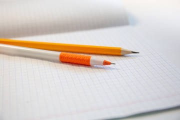 School tools. Orange pen and yellow pencil lie on on a notebook in a cage. Office and school tools.