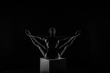 Girl yogi performs exercises on a black background. Space for text. The flexibility of the female body. Asana. Relief of the muscles. Figures from the body.