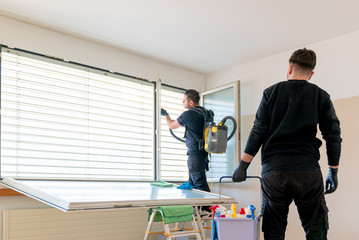 professional cleaning team in an apartment cleaning windows and blinds with a vacuum and other cleaning equipment