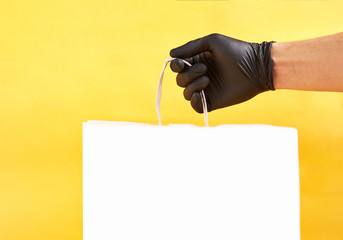 Man's hand holds white paper package on a yellow background. Delivery. Space for text