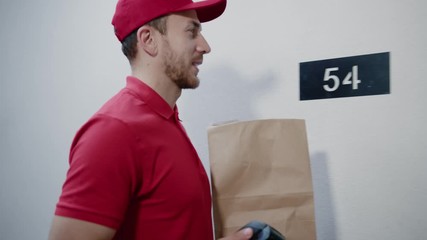 Handsome caucasian courier carries food package and cash machine arriving at customer house. Beautiful young woman receiving delivery using paypass NFC technology paying for order.