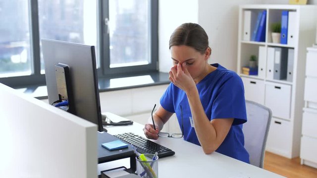 medicine, technology and healthcare concept - tired female doctor or nurse in glasses with computer working at hospital