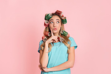 Pensive housewife in curlers presses finger to cheek and looks up