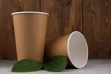 Two eco-friendly cardboard cups with green leaves lie on a concrete surface on a wooden background.Mock-up. Close-up.