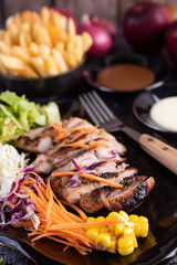 Sliced ​​pork steak with bread, carrots, cauliflower, lettuce and corn on a black plate.