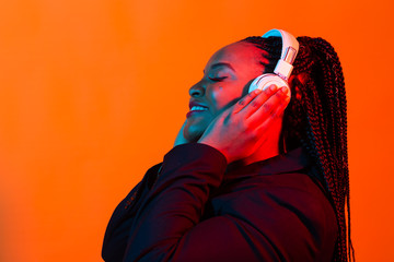 Neon portrait of young african woman listening music with earphones.