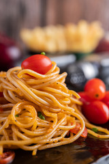 Spaghetti in a black cup with tomatoes and lettuce.