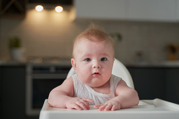 cute blond child sits in a children's chair at the kitchen and eat a juicy peach. Little girl with a piercing look