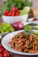 Spicy minced chicken on a white plate complete with cucumber, lettuce and side dishes.