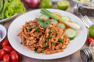 Spicy minced chicken on a white plate complete with cucumber, lettuce and side dishes.