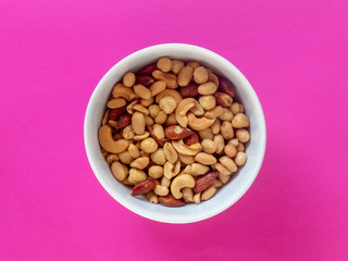 A bowl of a roasted nut mix isolated on a pink background