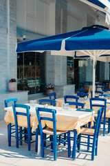 Romantic Greek restaurant with blue chairs and tables under palm leaves, Greece
