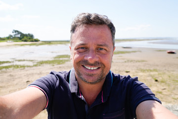 Man on vacation smiling at the beach taking selfie