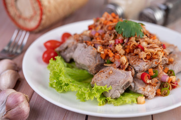 Spicy pork minced with tomatoes and lettuce on a white plate on a wooden table.