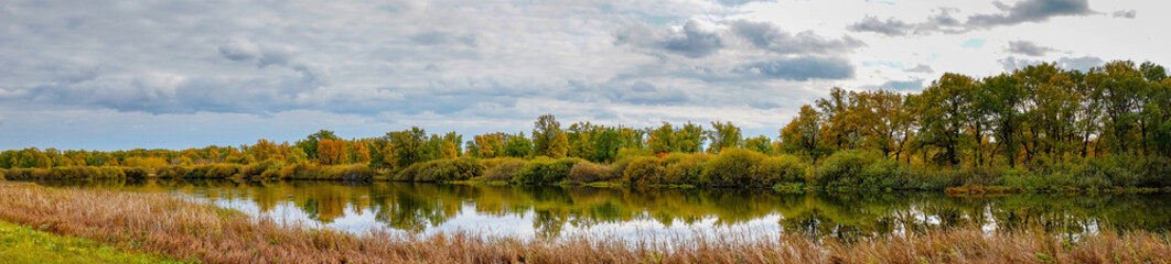 Panorama Overcast clouds over a small forest lake in front of a beautiful autumn forest. Autumn landscape