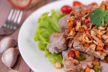Spicy pork minced with tomatoes and lettuce on a white plate on a wooden table.