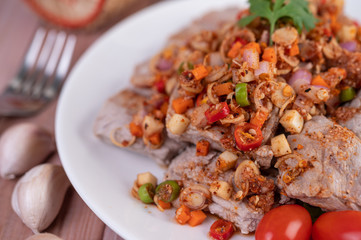 Spicy pork minced with tomatoes and lettuce on a white plate on a wooden table.