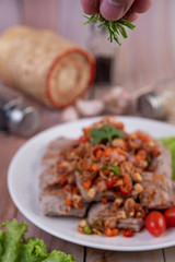 Spicy pork minced with tomatoes and lettuce on a white plate on a wooden table.